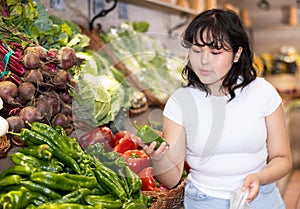 Attentive young woman purchaser choosing peppers in grocery store