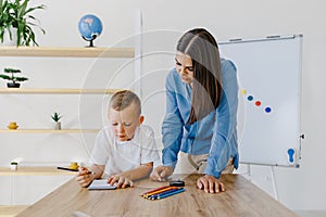 Attentive young woman tutor teacher helping little boy pupil with studying, correct mistakes explain learning material. Smiling