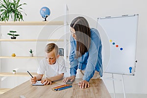 Attentive young woman tutor teacher helping little boy pupil with studying, correct mistakes explain learning material. Smiling