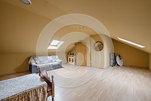 Attic bedroom of single family home with small wooden bed and ugly sofa under skylight, hardwood floor and round wood framed