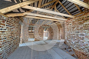 Attic of a building under construction with wooden beams of a roof structure and brick walls