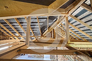 Attic of a building under construction with wooden beams of a roof structure and brick walls