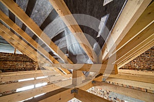 Attic of a building under construction with wooden beams of a roof structure and brick walls