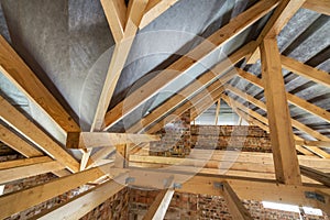 Attic of a building under construction with wooden beams of a roof structure and brick walls