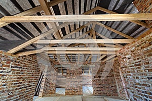 Attic of a building under construction with wooden beams of a roof structure and brick walls