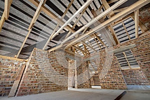 Attic of a building under construction with wooden beams of a roof structure and brick walls