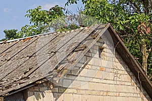 Attic of an old brown brick house with a small window and a broken gray slate roof on a rural street