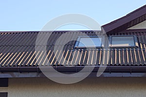 Attic of a private house with a brown slate roof and two windows on the street