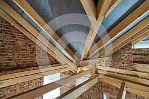 Attic space of a building under construction with wooden beams of a roof structure and brick walls. Real estate development