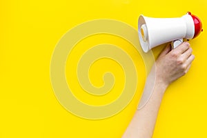 Attract attention concept. Megaphone in hand on yellow background top view copy space