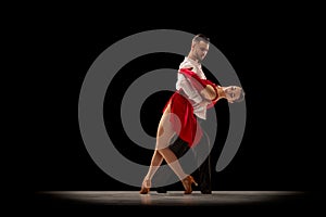 Attraction. Young man and woman, professional ballroom dancers, dancing tango over black background. Concept of art