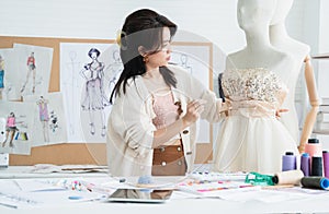 Attractive 30s woman fashion designer or dressmaker holding needle to fixing new evening dress collection on a mannequin, working