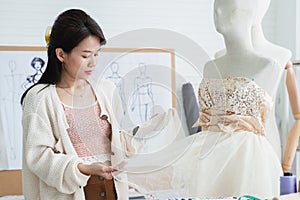 Attractive 30s woman fashion designer or dressmaker touching textile fabric texture on mannequin and thinking