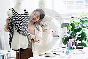 Attractive 30s woman fashion designer or dressmaker try to fitting new dress collection on a mannequin, working with happiness