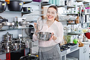 Attractive adult woman is buying new stewpot for kitchen in tableware shop