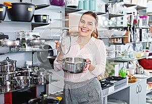 Attractive adult woman is buying new stewpot for kitchen in tableware shop