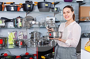 Attractive adult woman is buying new stewpot for kitchen in tableware shop