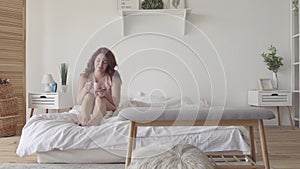 Attractive adult woman drinking tea or coffee sitting in bed in the morning. Smiling lady relaxing at home. Leisure