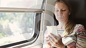 Attractive adult woman riding a train and reading a book on a mobile phone.