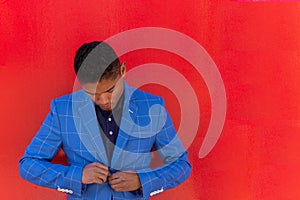 Attractive african american businessman in stylish suit is fastens his jacket and smiling, red background