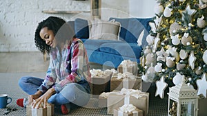 Attractive mixed race girl packing gift box near Christmas tree at home