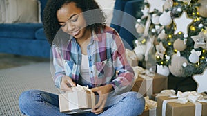 Attractive mixed race girl packing gift box near Christmas tree at home