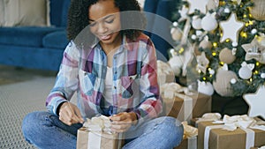 Attractive mixed race girl packing gift box near Christmas tree at home