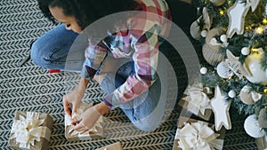 Top view of Attractive mixed race girl packing gift box near Christmas tree at home