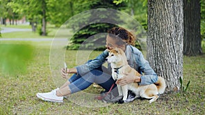 Attractive African American girl is taking selfie with cute dog resting in city park cuddling and caressing beautiful