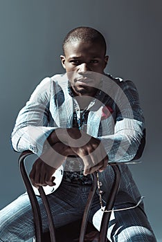 Attractive african american man in fashionable suit, sitting on chair backwards and looking at camera,