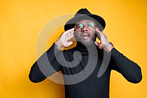 Attractive african american man in glasses in a hat touches his head with his hands and opens his mouth