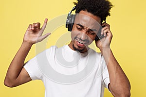 Attractive African American man with headphones listen to music. Isolated over yellow gold background.