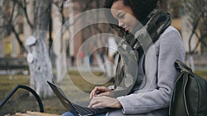 Attractive african american student girl typing on laptop computer sitting on bench near univercity photo