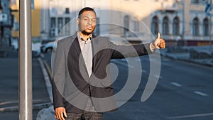 Attractive African American student, young guy in suit waiting for cab outdoors. Modern businessman or manager gesturing