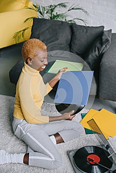 Attractive african american woman holding vinyl record and sitting