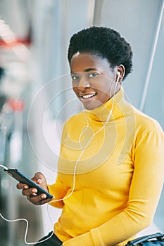 Attractive African girl is waiting for a train in the subway and listening to music with headphones