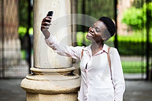 Attractive afro american young woman blogger dressed in trendy casual outfit making selfie via smartphone to share with followers