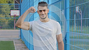 Attractive Arab bearded athletic guy in white T-shirt shows big manly muscles, demonstrates triceps. Young energetic