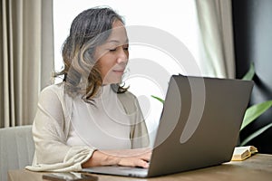 Attractive Asian-aged woman or female entrepreneur working from home, using laptop