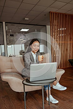 Attractive asian business woman working laptop and drink coffee sitting in cozy office
