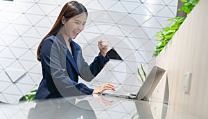 An attractive Asian businesswoman girl expressing a winning moment. Worker working on laptop at the office showing her confidence