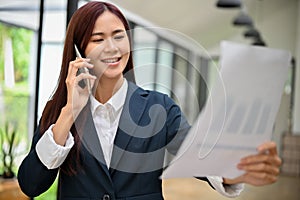 Attractive asian businesswoman reading a financial report paperwork and talking on the phone