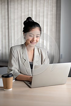 An attractive Asian businesswoman responding to emails on her laptop while working at her desk