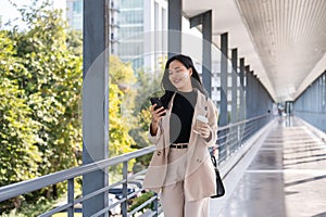 An attractive Asian businesswoman is responding to messages on her phone while walking on a skywalk