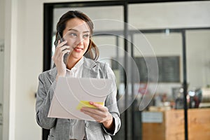 Attractive Asian businesswoman talking on the phone with someone, holding a document