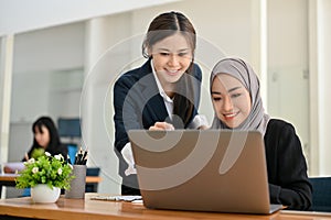 Attractive Asian businesswoman training and giving an advice to her Muslim colleague in the office