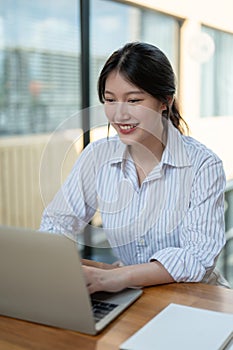 An attractive Asian businesswoman is working on her laptop in a modern office or co-working space