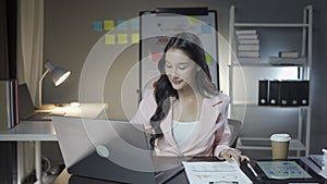 Attractive Asian businesswoman working with laptop and checking financial documents and analyzing company