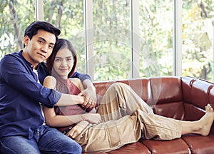 Attractive Asian couple spend time together , a woman sitting on couch leaning on her boyfriend hugging her from back and looking