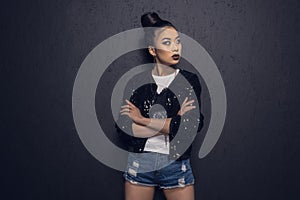 Attractive asian disco girl with crossed arms looking away and posing at grey wall in studio